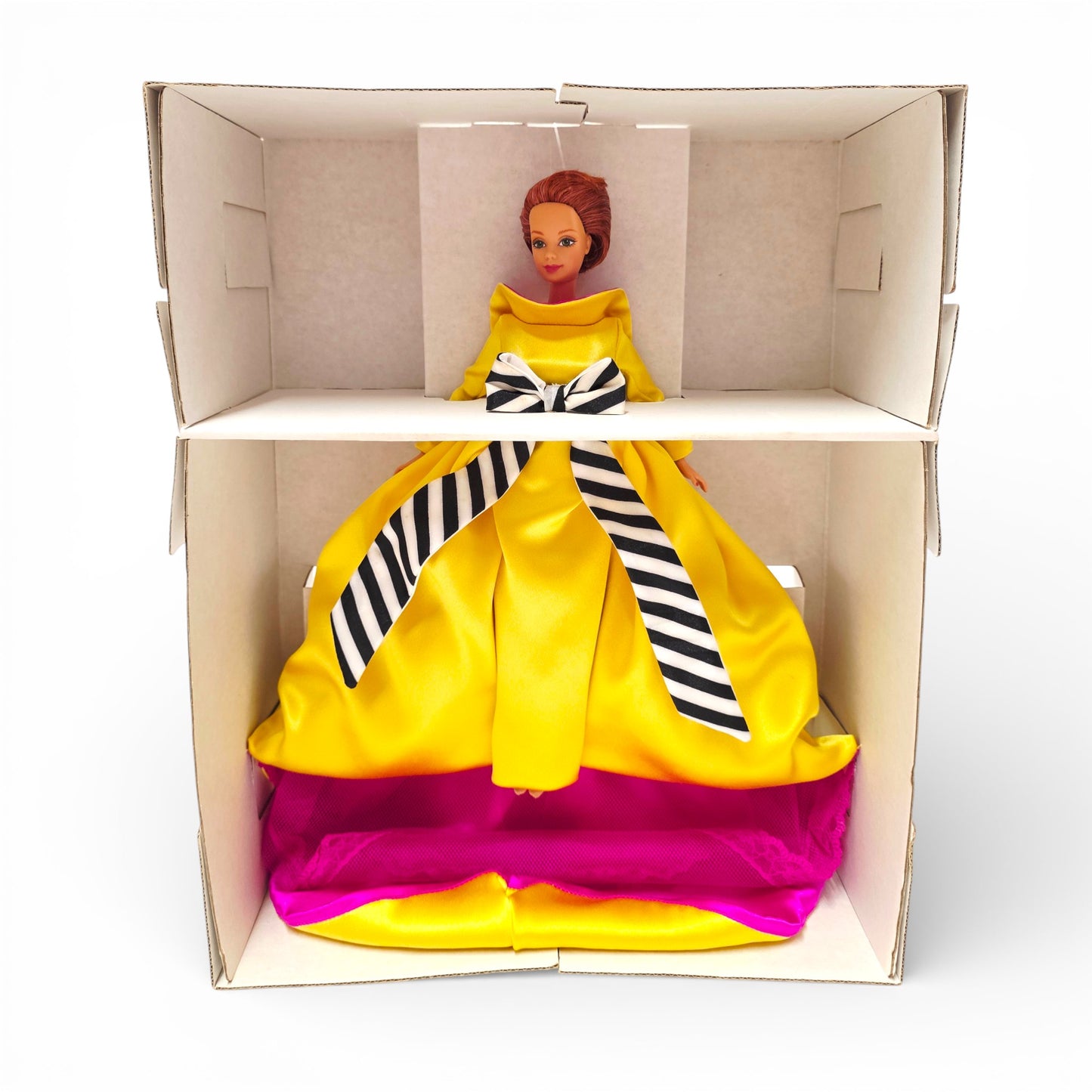 Barbie doll in a yellow dress with a striped bow in an open cardboard box.